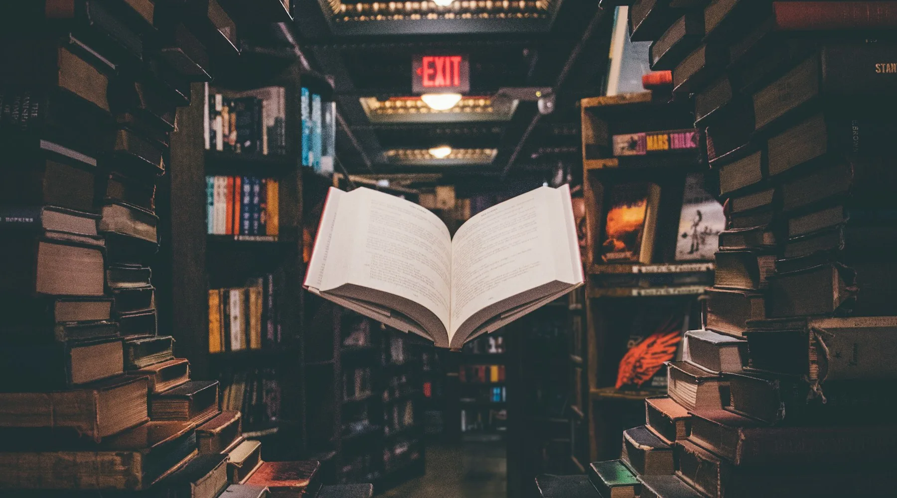 Carte deschisă pe culoarul unei librării, rafturi pe ambele părți, lectură după o distopie de supraveghere